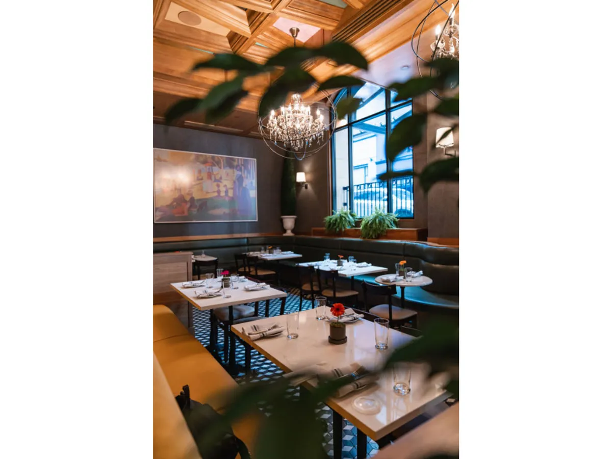 A cozy, sophisticated dining room with a stunning chandelier, curated artwork, lush plant arrangements, and elegantly set tables. The setting balances artistic flair with comfort, ideal for socializing or winding down after a day of activity.