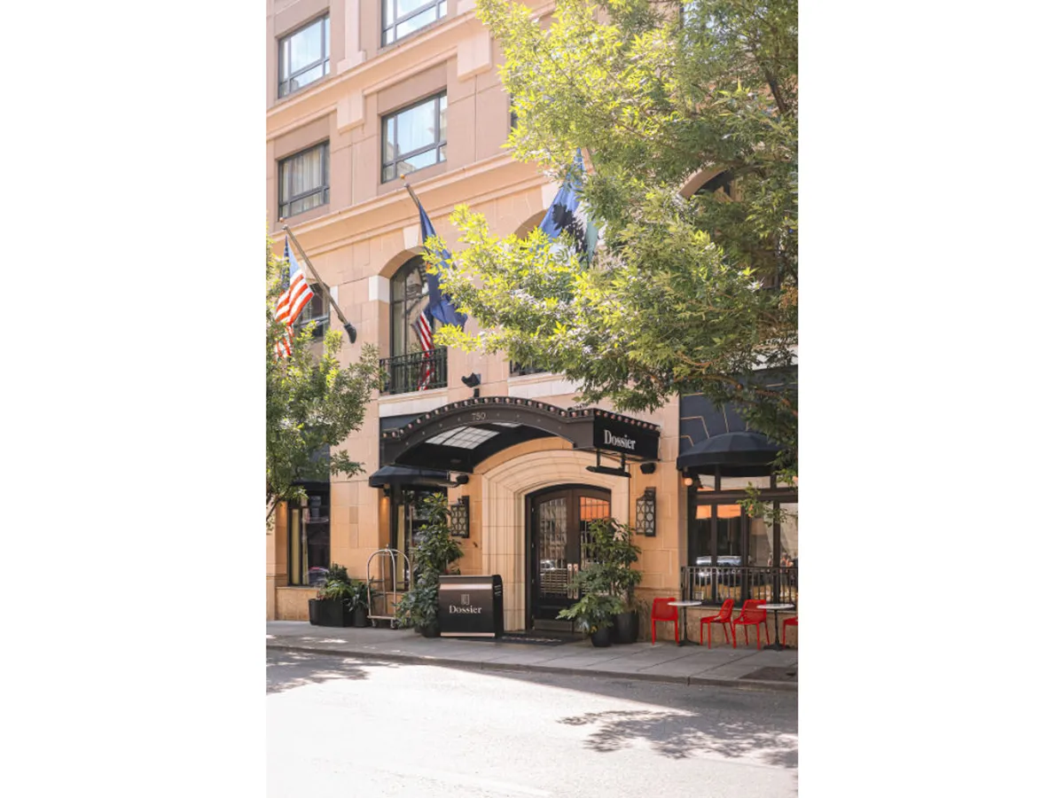 This image captures the hotel’s exterior entrance, featuring a welcoming awning, flags, planters, and outdoor seating. Guests are seen dining outdoors and socializing, creating a lively urban atmosphere that reflects the energy of Portland’s city life just outside the hotel.